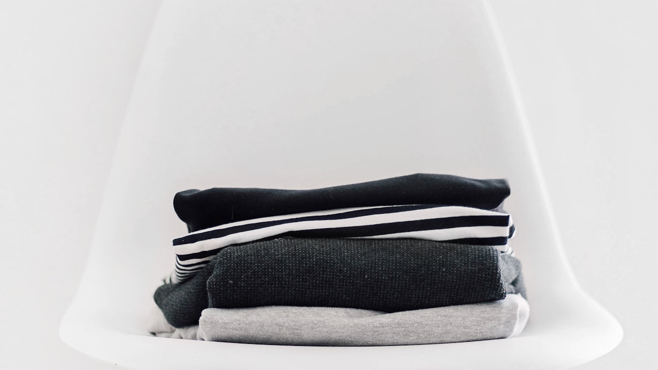 A folded pile of neutral everyday tops, the clothing a fabric label decides the quality of